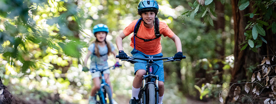 2 kids riding bikes down a forested path