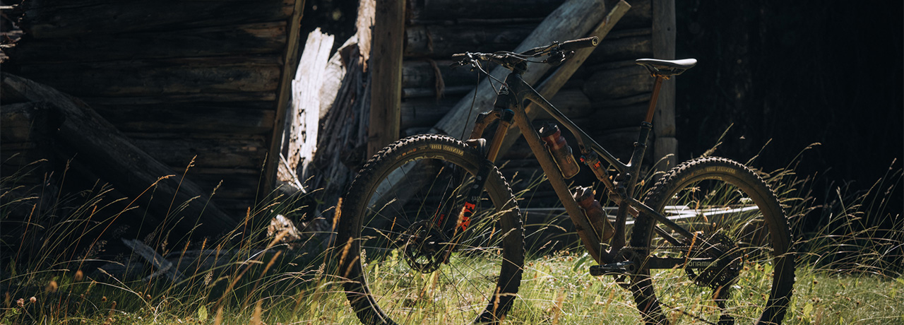 rocky mountain brand mountain bike staged on its own in the grass in front of an old log cabin