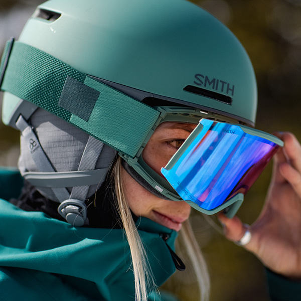 woman wearing a teal Smith Helmet and teal Smith goggles changing out her goggle lens