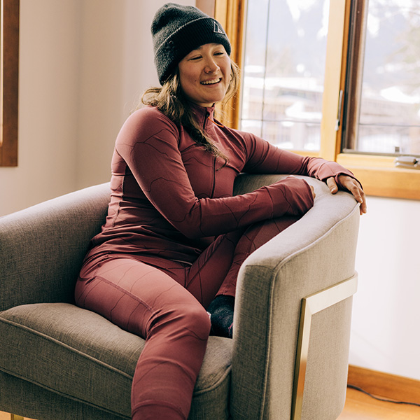 Woman sitting in a chair wearing dark pink Orage brand base layers and a black beanie hat