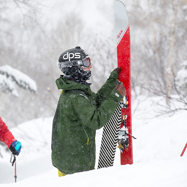 Skier holding up red DPS skis with touring skins standing in the snow