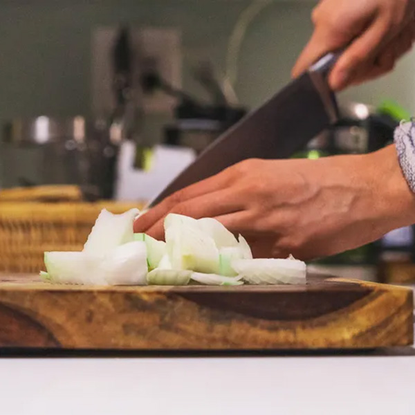 close view of a butchers knife chopping a yellow onion on a wooden cutting board