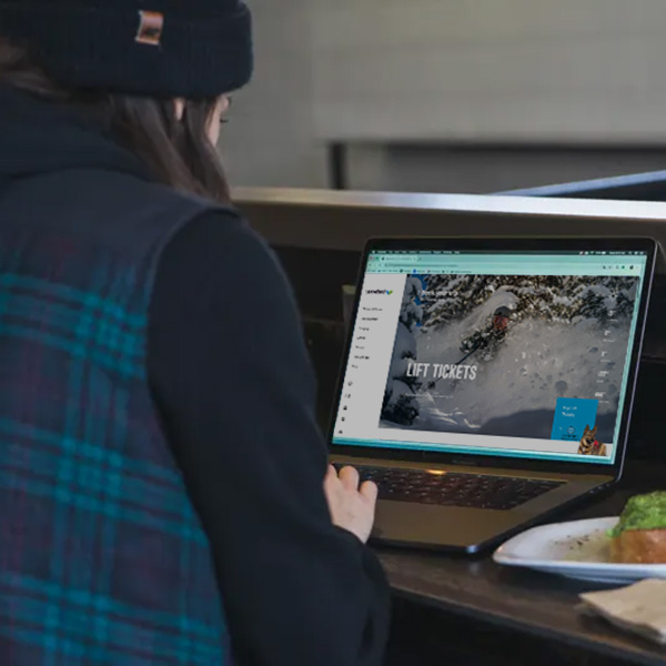 woman in a blue flannel researching ski lift tickets on her laptop