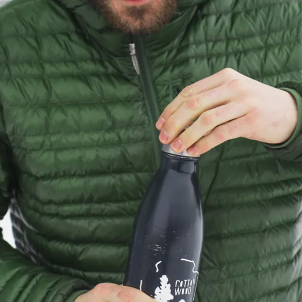 close up of a person wearing a green puffy coat holding a black water bottle