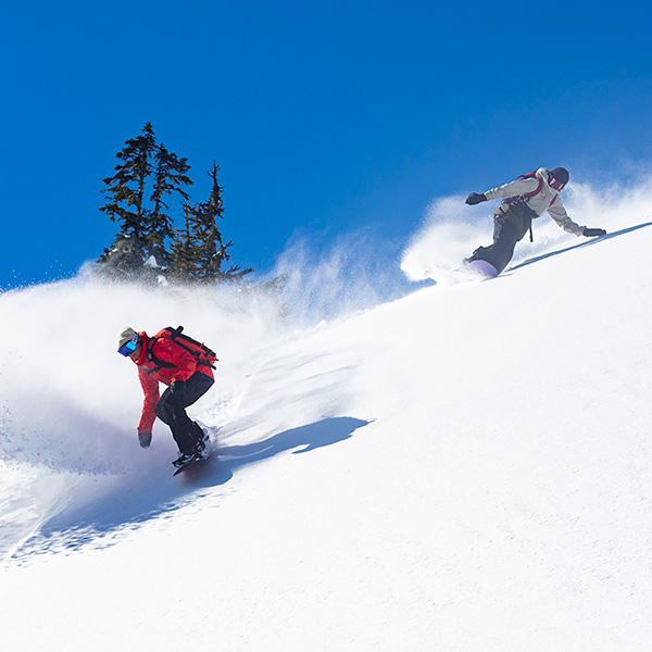 two snowboarders riding down a snowy slope with blue skies