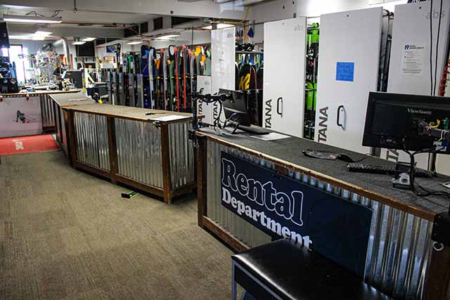 A rental counter with ski racks behind it holding rental