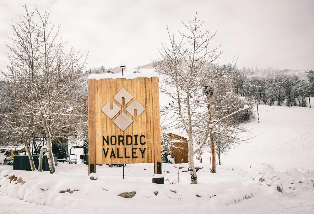 Nordic valley sign is covered with snow in the foreground. in the background is a snow covered ski hill.